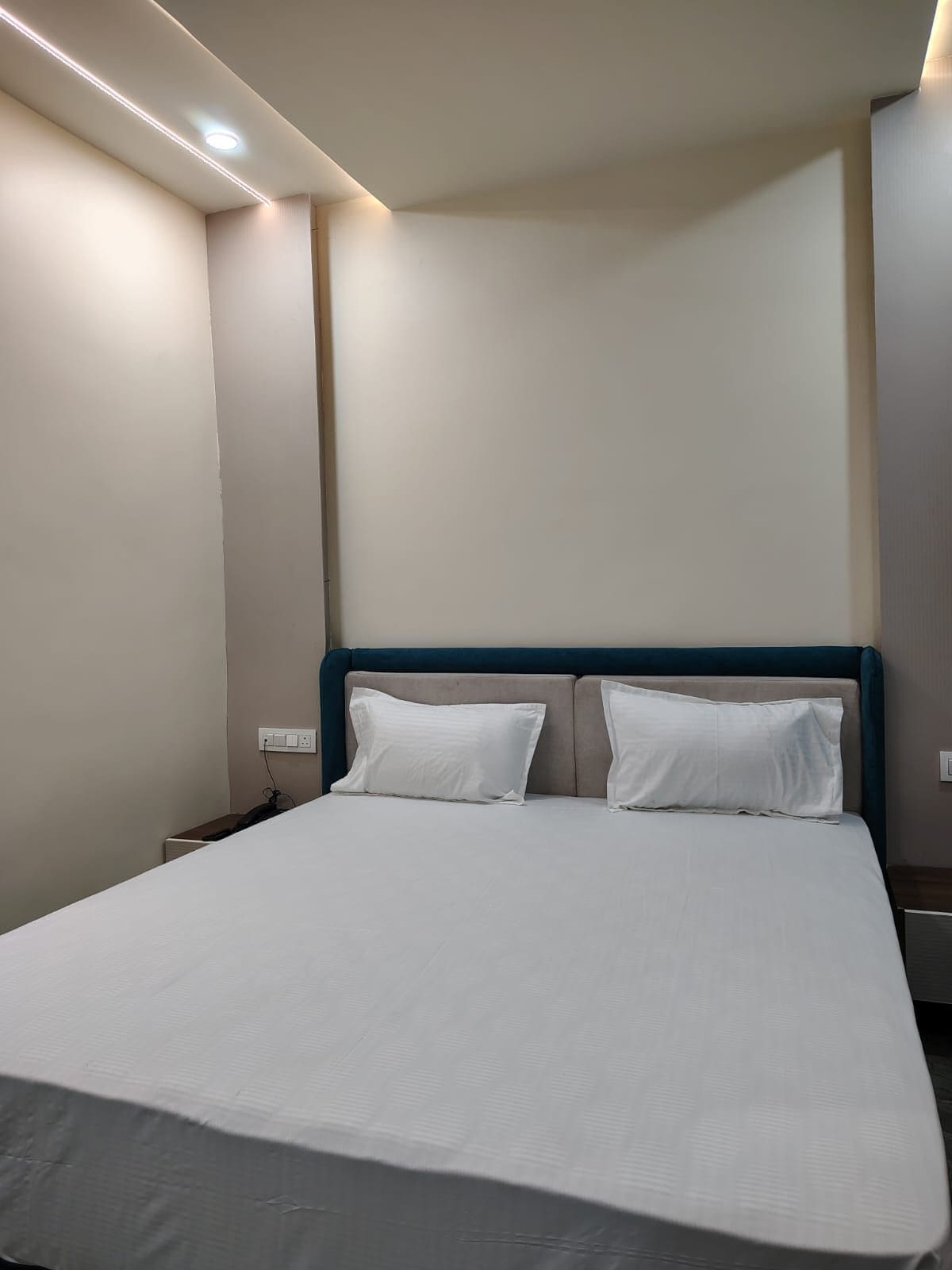 A hotel room with a large bed, a nightstand, and a wall socket.