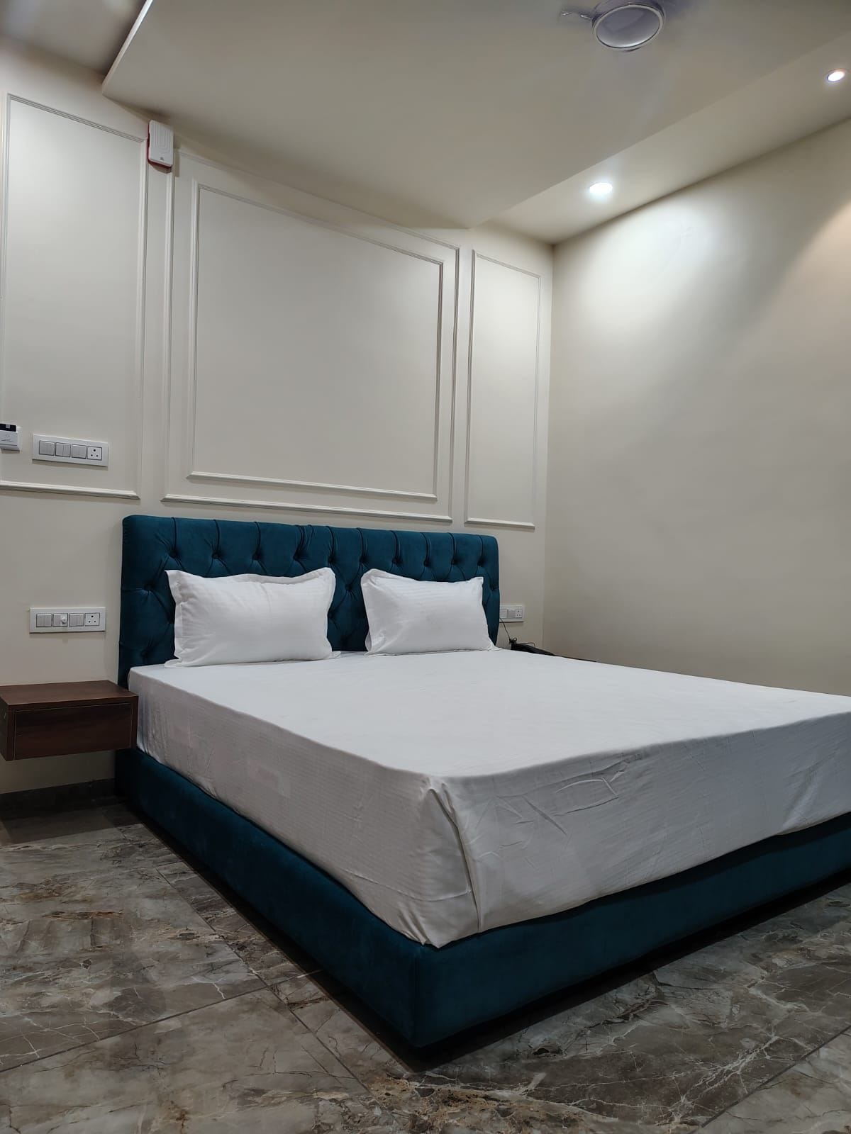 Un dormitorio con una cama grande, ropa de cama blanca, un cabecero tapizado en color aguamarina y suelo de mármol.