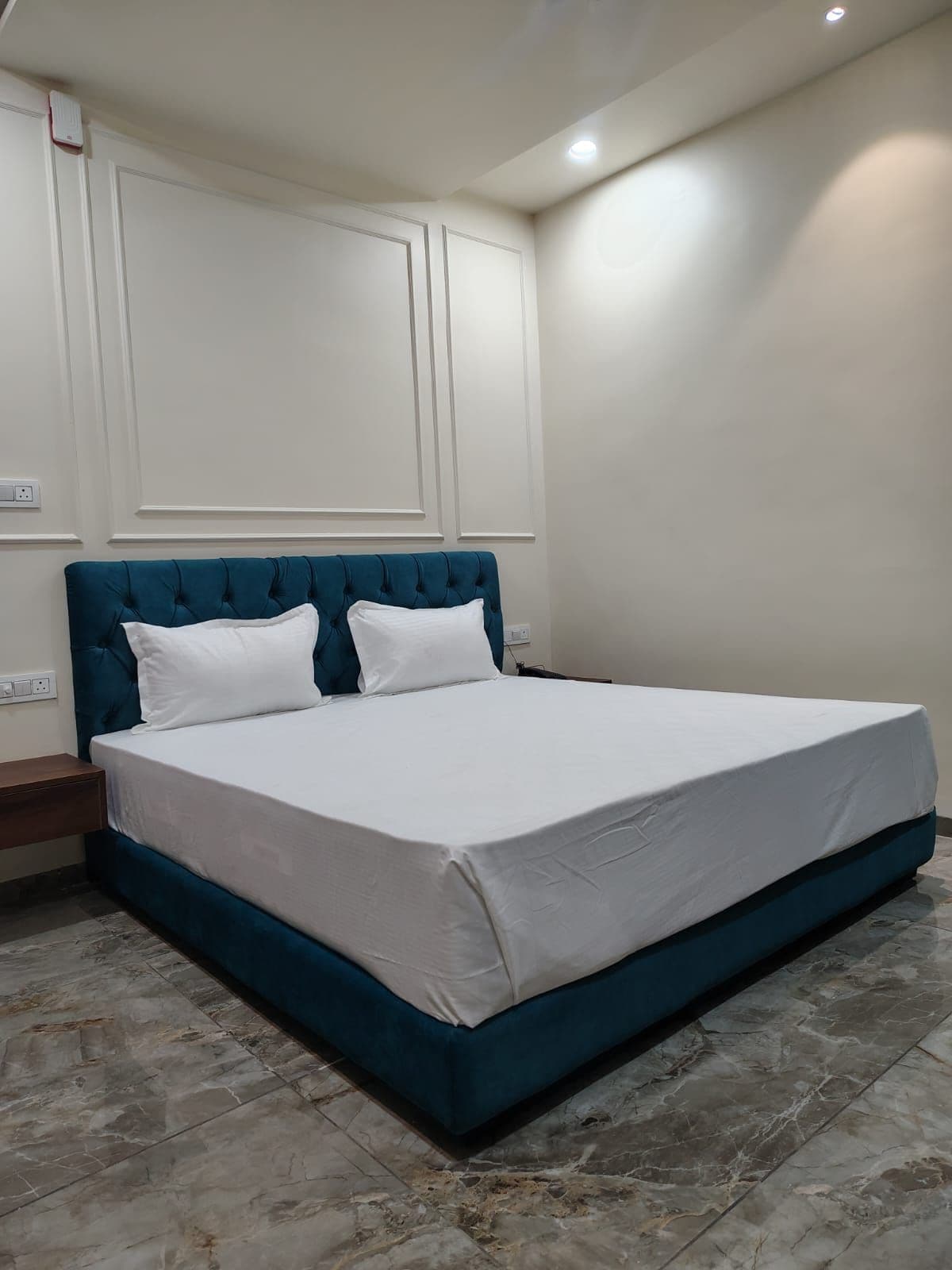 Een slaapkamer met een groot bed, wit beddengoed, een blauwgroen hoofdeinde en een marmeren vloer.