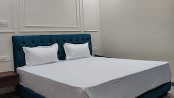 Een slaapkamer met een groot bed, wit beddengoed, een blauwgroen hoofdeinde en een marmeren vloer.