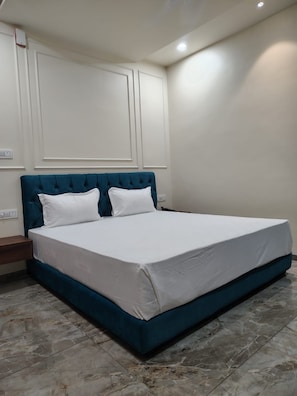 Een slaapkamer met een groot bed, wit beddengoed, een blauwgroen hoofdeinde en een marmeren vloer.