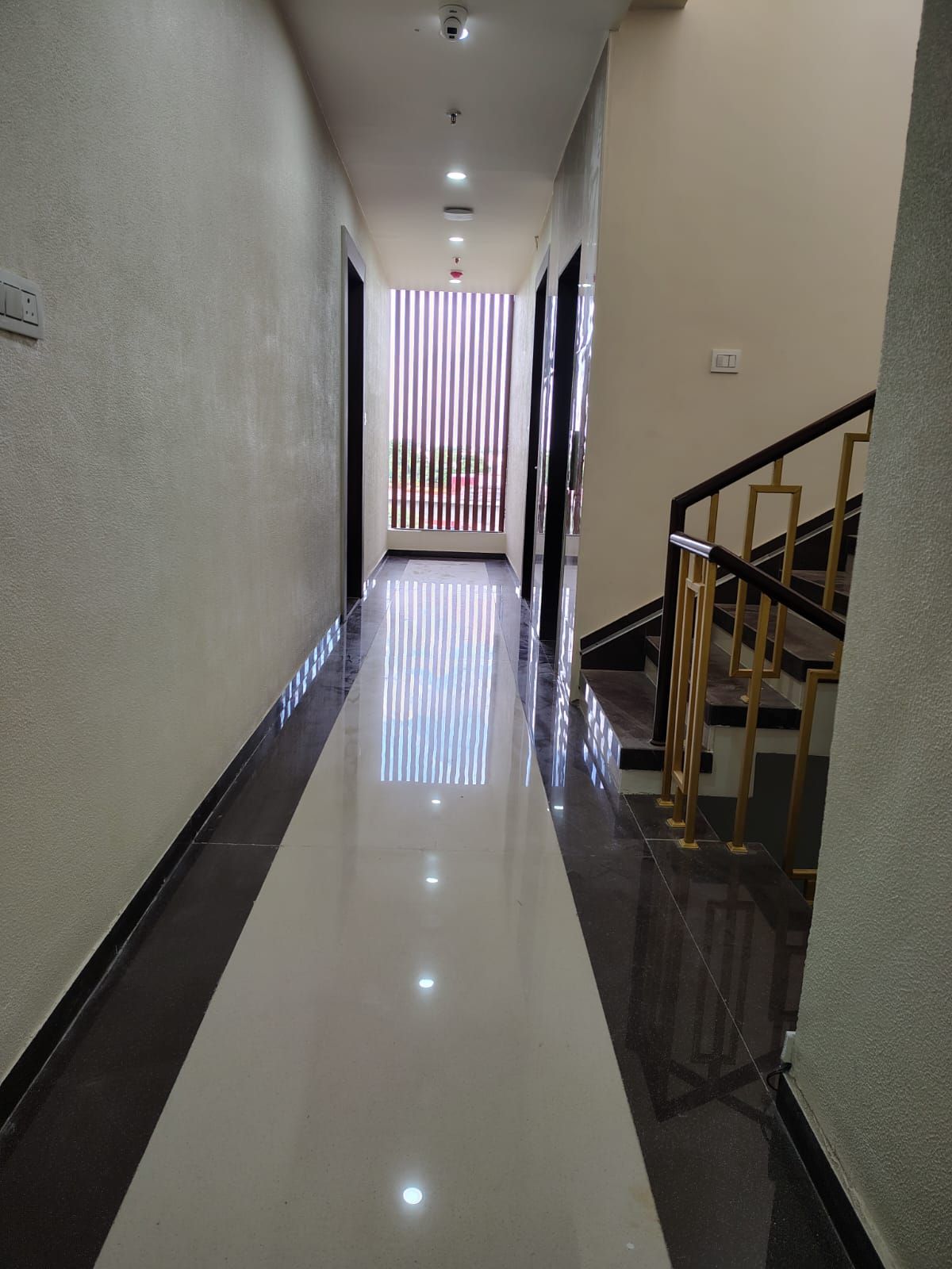 A hallway with a reflective floor leading to a staircase with a handrail.