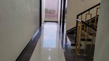 A hallway with a reflective floor leading to a staircase with a handrail.