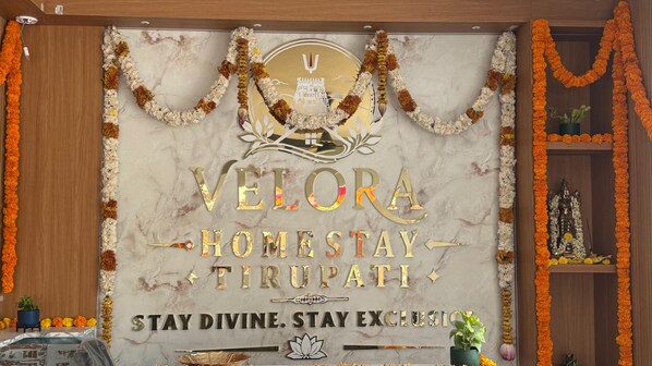 A marble wall with gold lettering and a central emblem, surrounded by floral garlands. - VELORA HOME STAY (Tirupati)