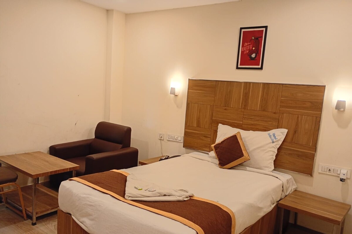 A hotel room with a bed, a wooden headboard, a brown leather armchair, a small wooden table, and a nightstand.