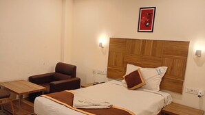 A hotel room with a bed, a wooden headboard, a brown leather armchair, a small wooden table, and a nightstand. - VELORA HOME STAY (Tirupathi)