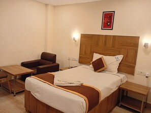 A hotel room with a bed, a wooden headboard, a brown leather armchair, a small wooden table, and a nightstand. - VELORA HOME STAY (Tirupathi)