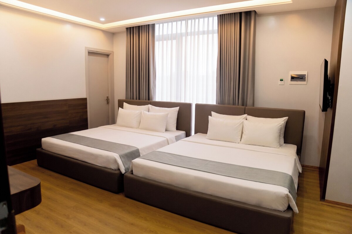 Habitación de hotel con dos camas, cabecero de madera, televisor y ventana con cortinas.