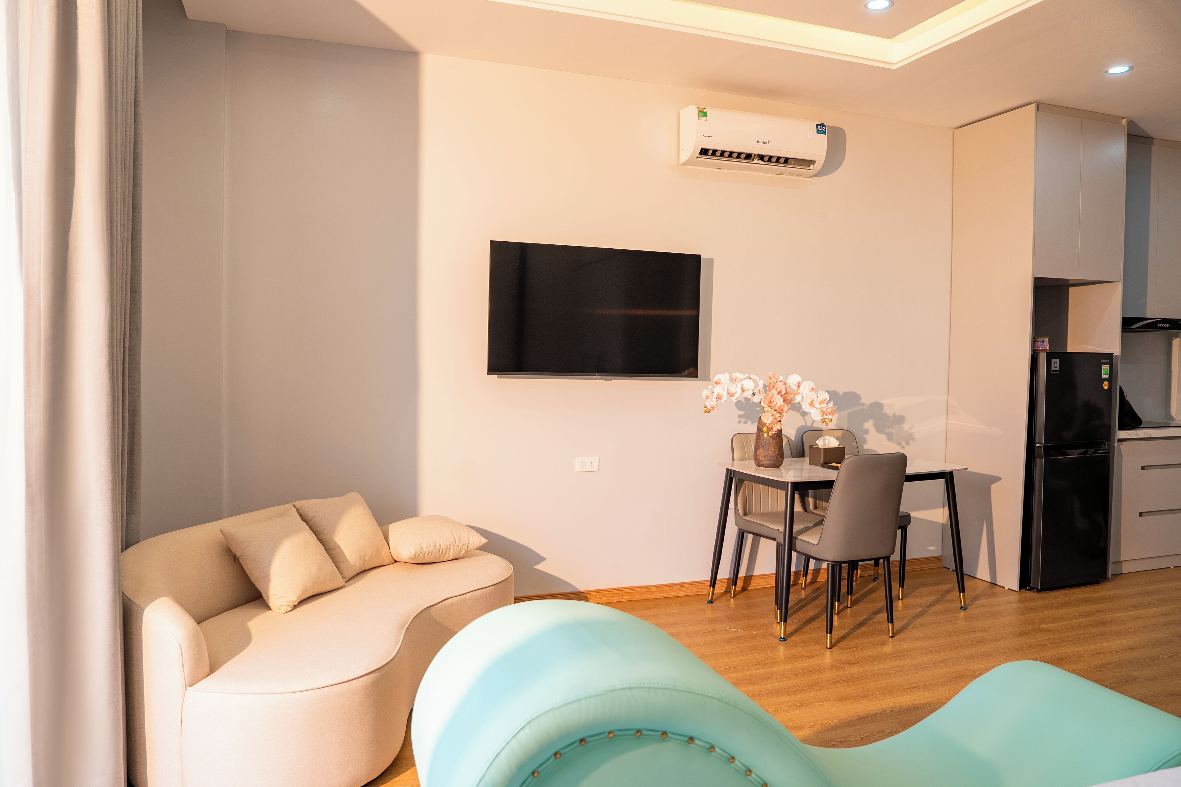 Een moderne woonkamer met een bank, een televisie, een eethoek met stoelen en een keuken met een koelkast.