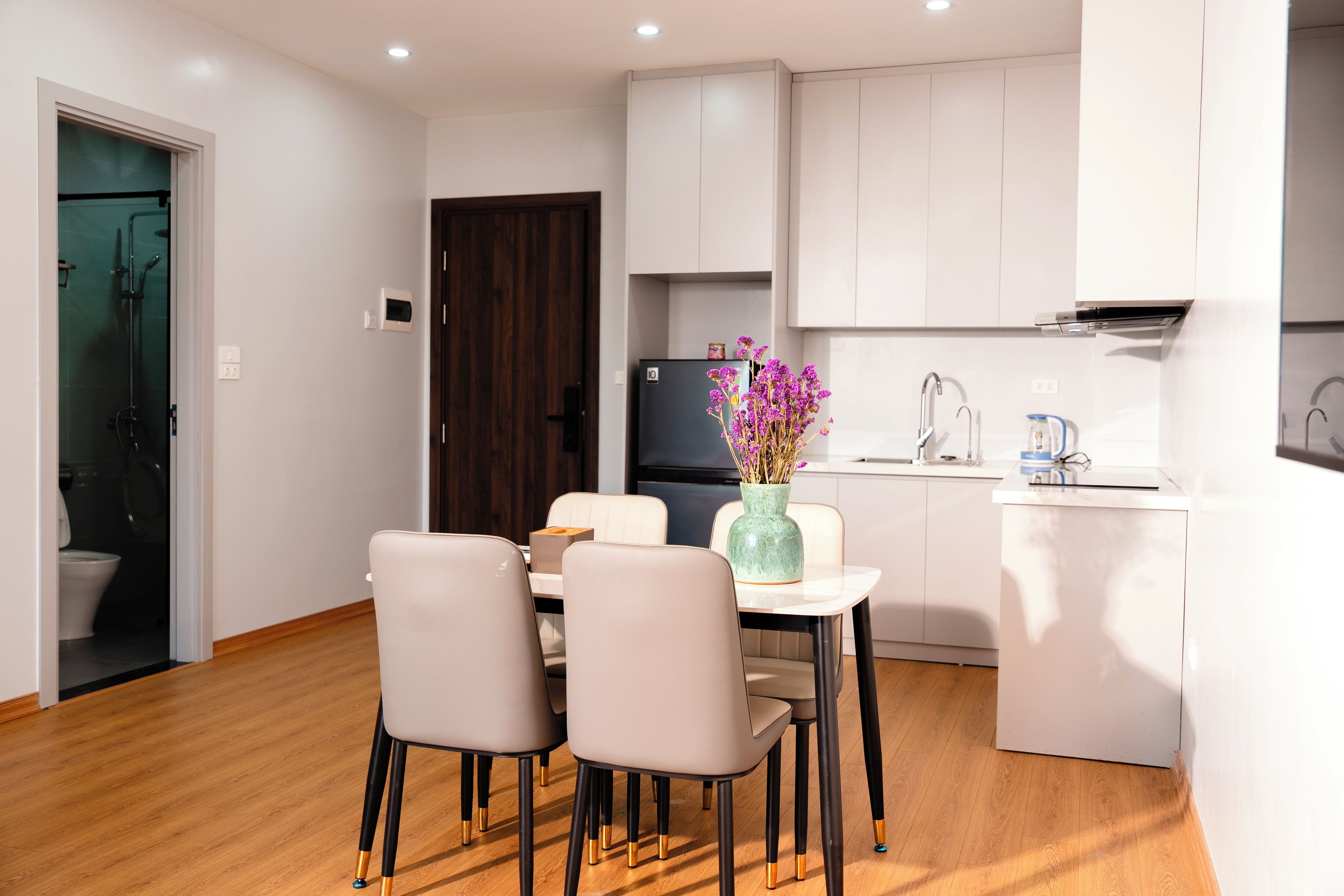 A modern kitchen with white cabinets, a dining table with chairs, and a vase with purple flowers.
