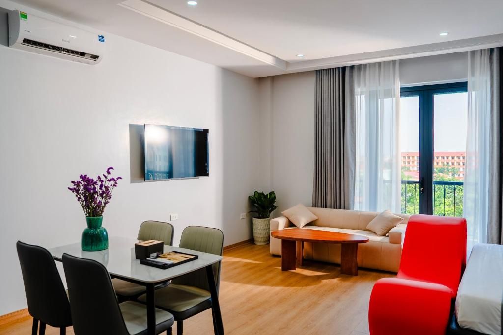 A modern living room with a dining area, a flat-screen TV mounted on the wall, a sofa, a red chair, and a balcony with a view.