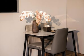 A dining area with a table, chairs, a vase with flowers, and a wall-mounted television.