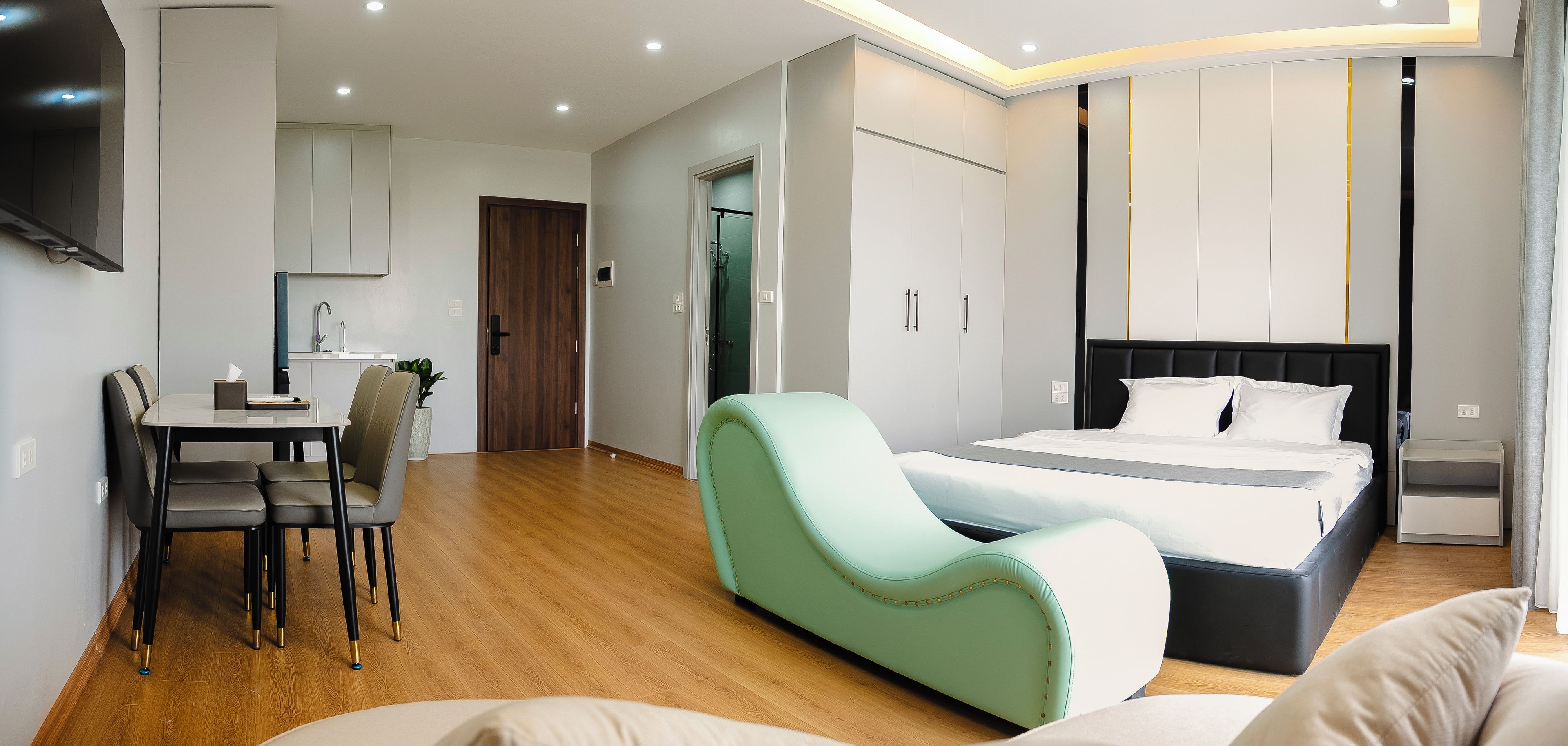 Een moderne hotelkamer met een bed, een zithoek, een tafeltje en een kitchenette.