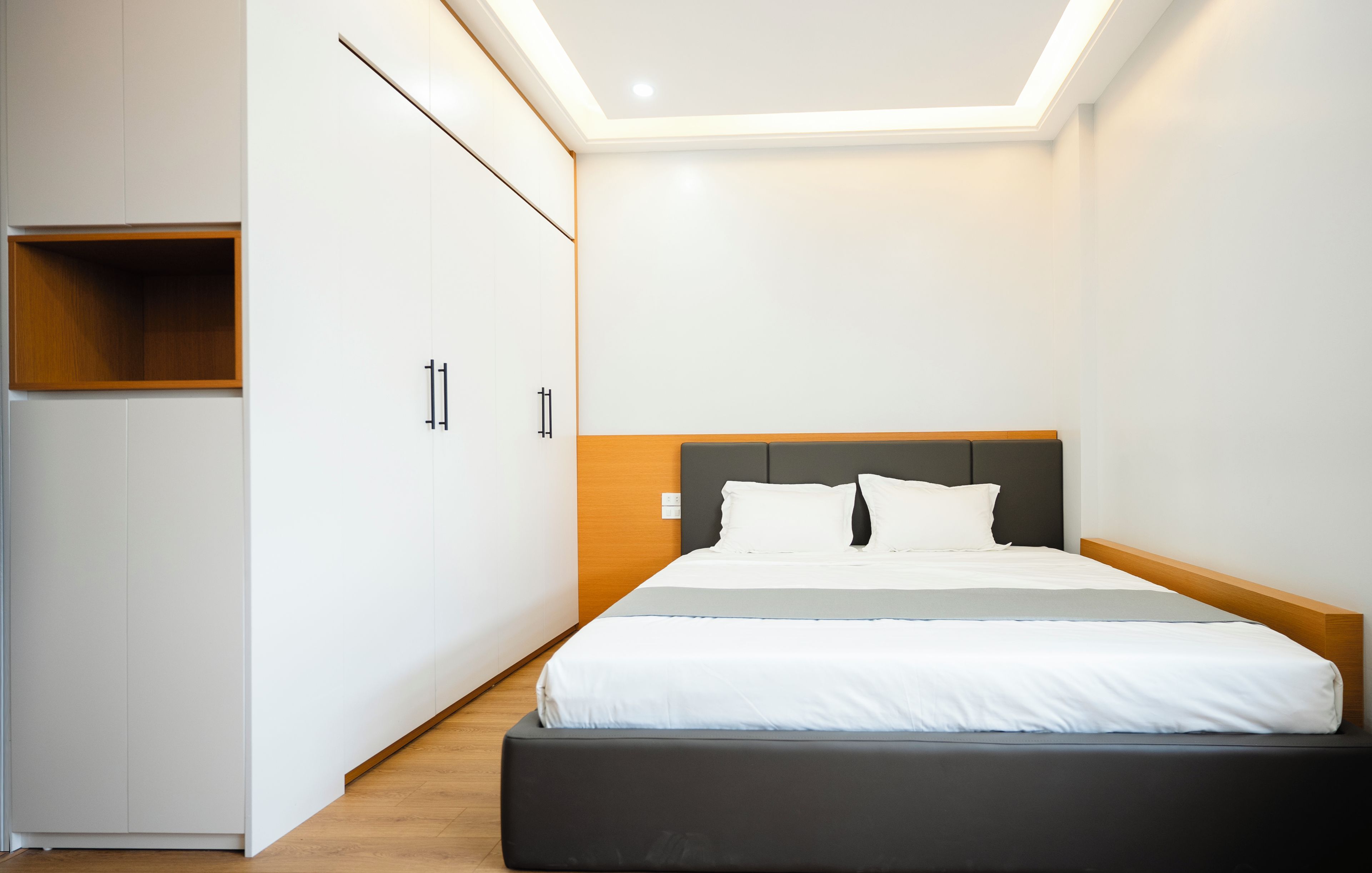 A modern bedroom with a bed, a wardrobe, and a built-in shelf.