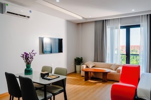 Una sala moderna con comedor, un televisor de pantalla plana montado en la pared, un sofá, un sillón rojo y una planta en maceta.