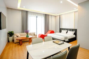 Una habitación de hotel moderna con una cama, un sofá, una mesa de comedor y una mesita con un jarrón de flores.