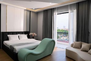 A hotel room with a bed, a lounge chair, a sofa, a balcony with a view, and a large window. - Lumia Hotel Vinh Yen (Vĩnh Phúc)