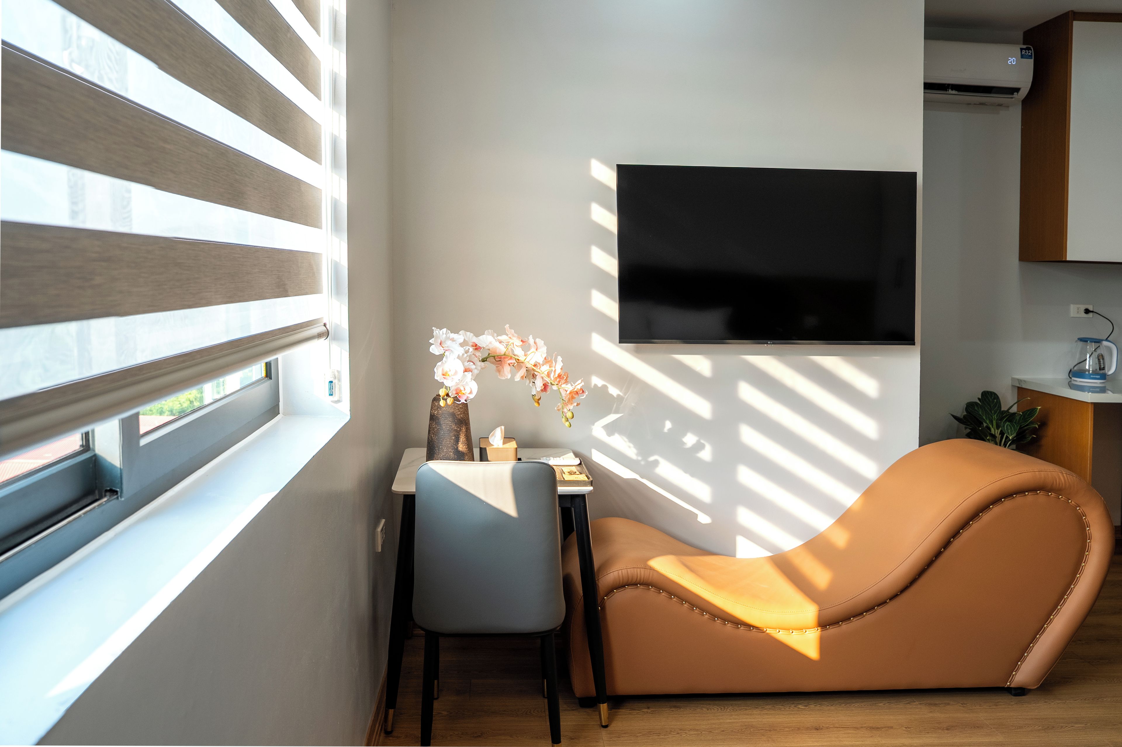 A modern living room with a sofa, a small table with a vase of flowers, and a flat-screen TV mounted on the wall.