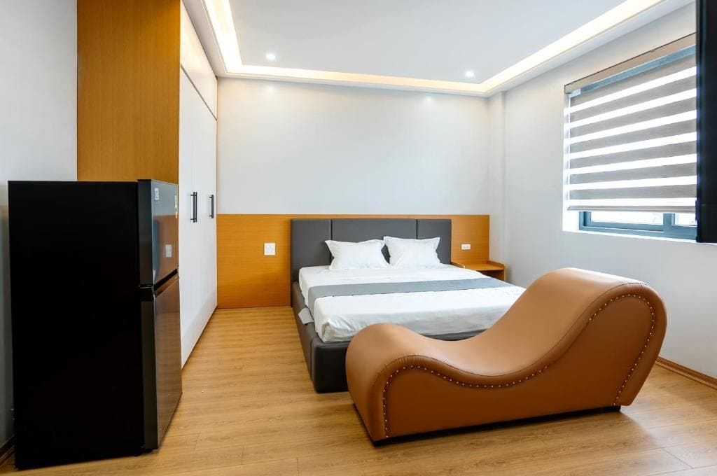 Un dormitorio con cama, sofá, refrigerador y ventana con persianas.