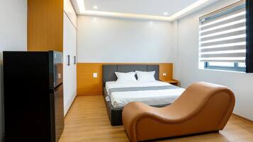 Un dormitorio con cama, sofá, refrigerador y ventana con persianas.