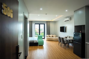 Una habitación de hotel moderna con cama, sofá, mesa de comedor con sillas, televisor montado en la pared y equipo de aire acondicionado.