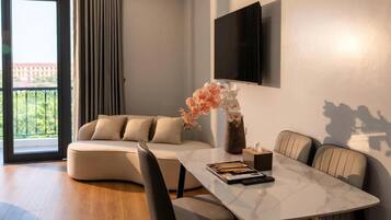 A modern living room with a sofa, a dining table, and a TV mounted on the wall.