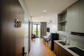 A modern kitchen with a built-in stove, a dining area with a table and chairs, and a view of the outdoors through a glass door. - Lumia Hotel Vinh Yen (Vĩnh Phúc)