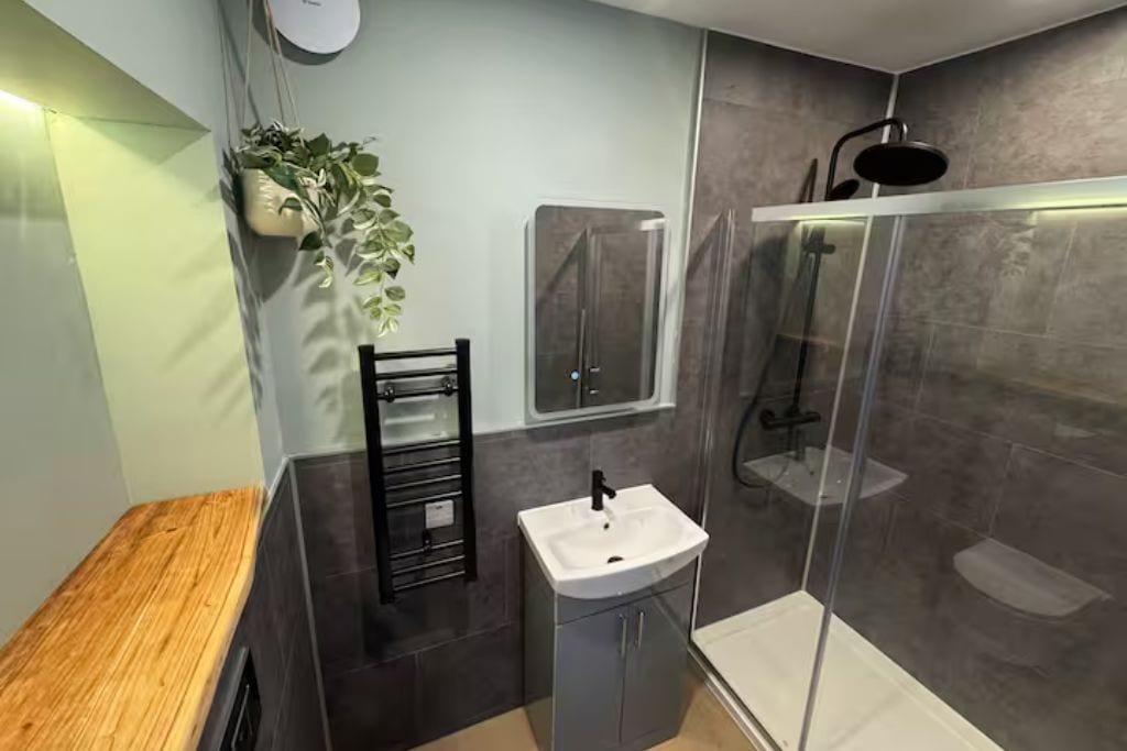 Ein modernes Badezimmer mit einer Holzbank, einem Waschbecken, einer Duschkabine aus Glas und einem Blumentopf.