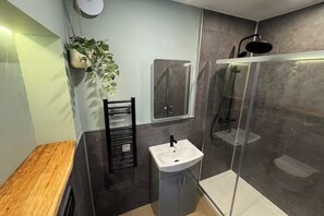 Un baño moderno con un banco de madera, un lavabo, una cabina de ducha de vidrio y una planta en maceta.