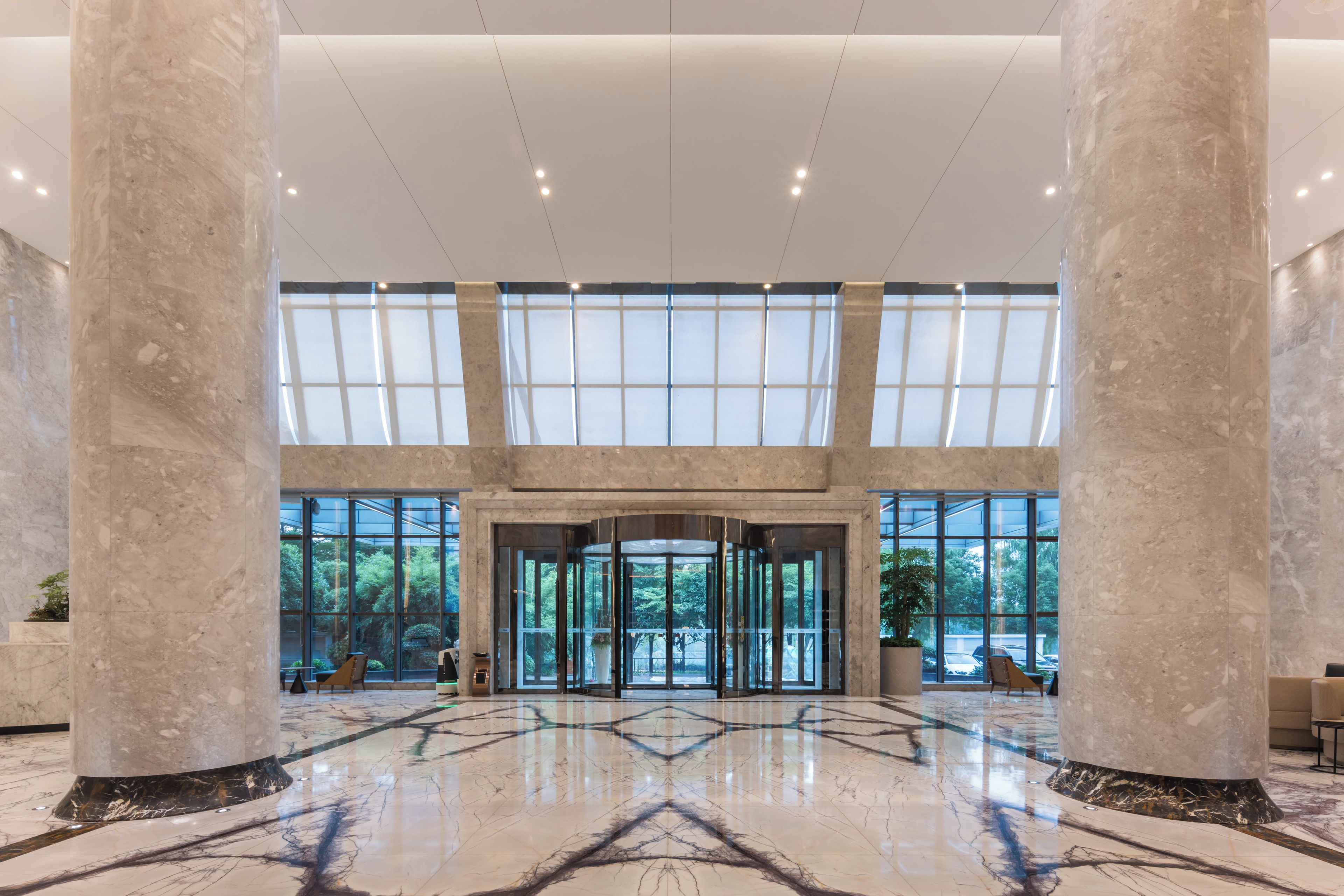 A spacious lobby with marble flooring, large glass doors, and a high ceiling.
