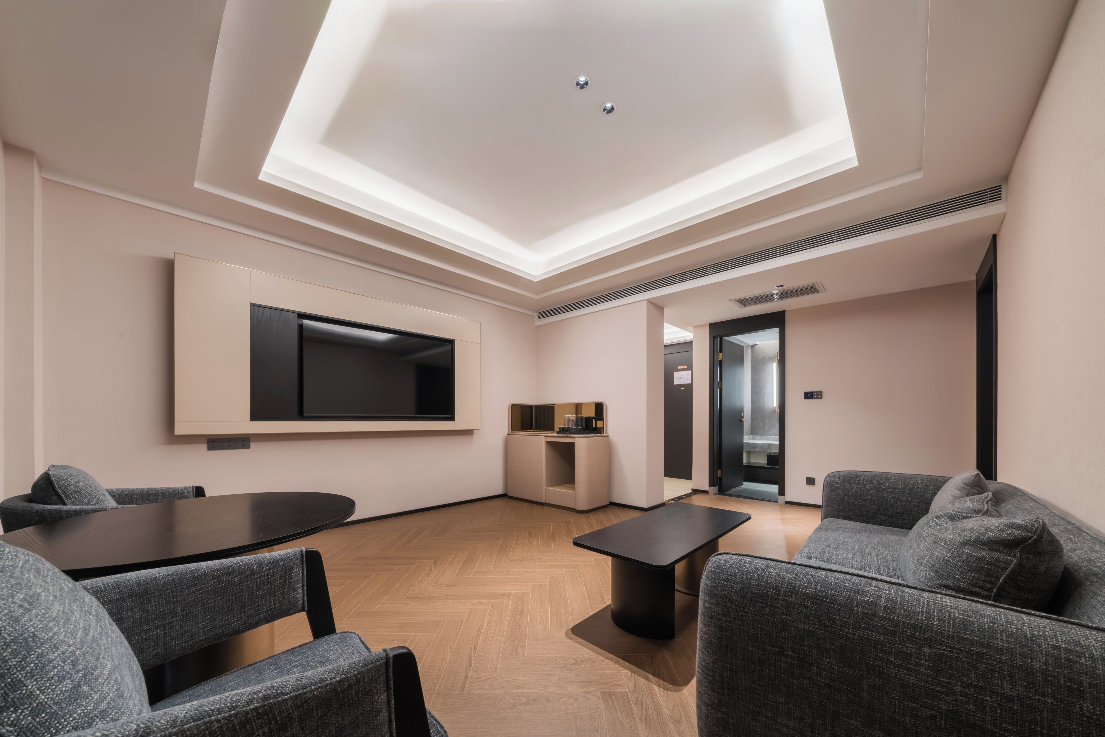 A modern interior with a flat-screen TV mounted on the wall, a small kitchenette, and a seating area with a table and chairs.