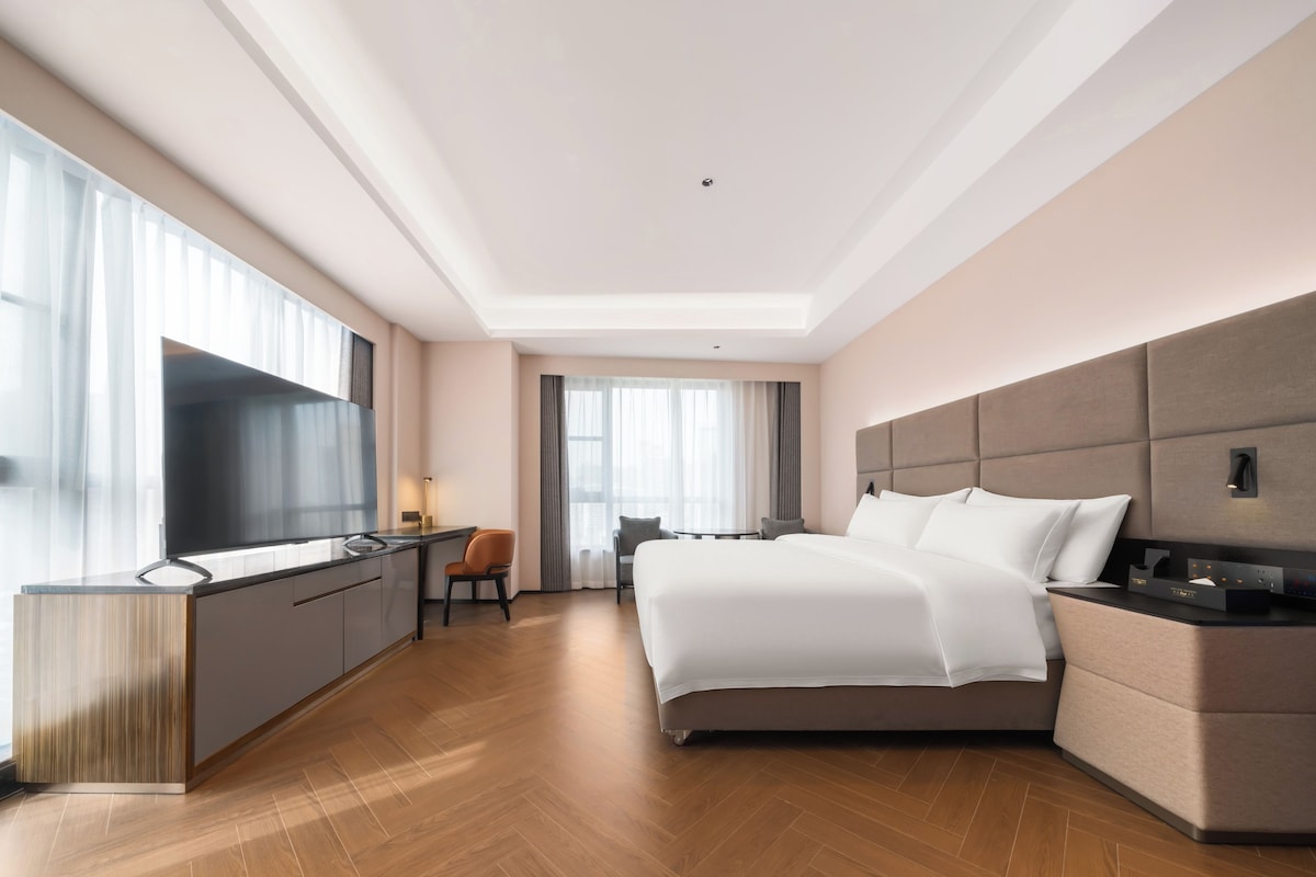 A modern hotel room with a large bed, a desk, and a television.