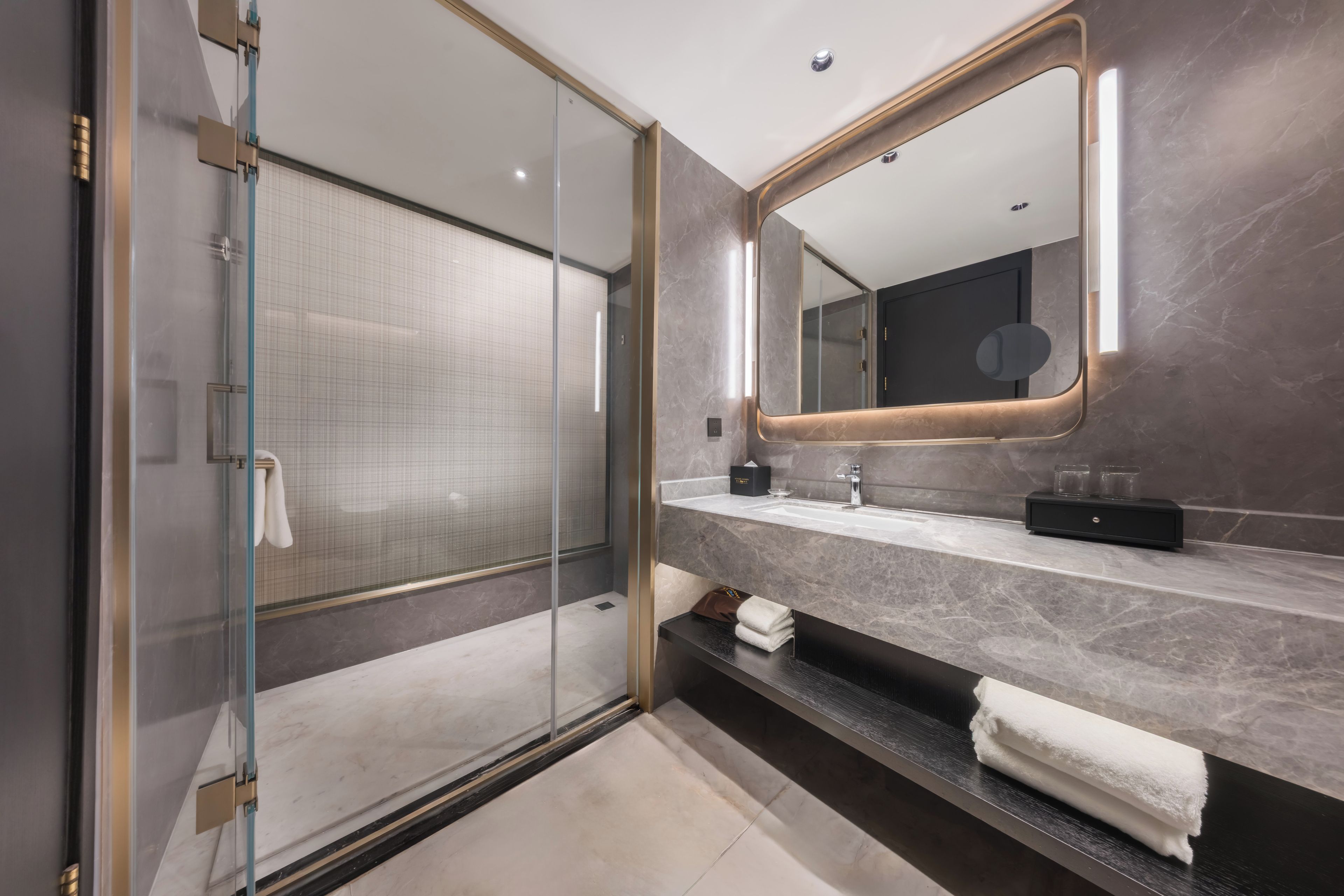 Un baño moderno con ducha de vidrio, un espejo grande y una encimera de mármol.