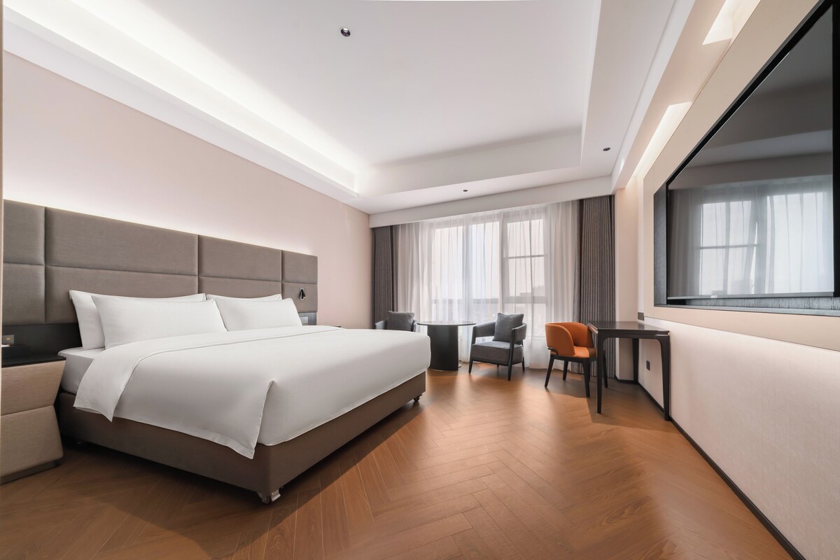 A modern hotel room with a large bed, a desk, and a chair.