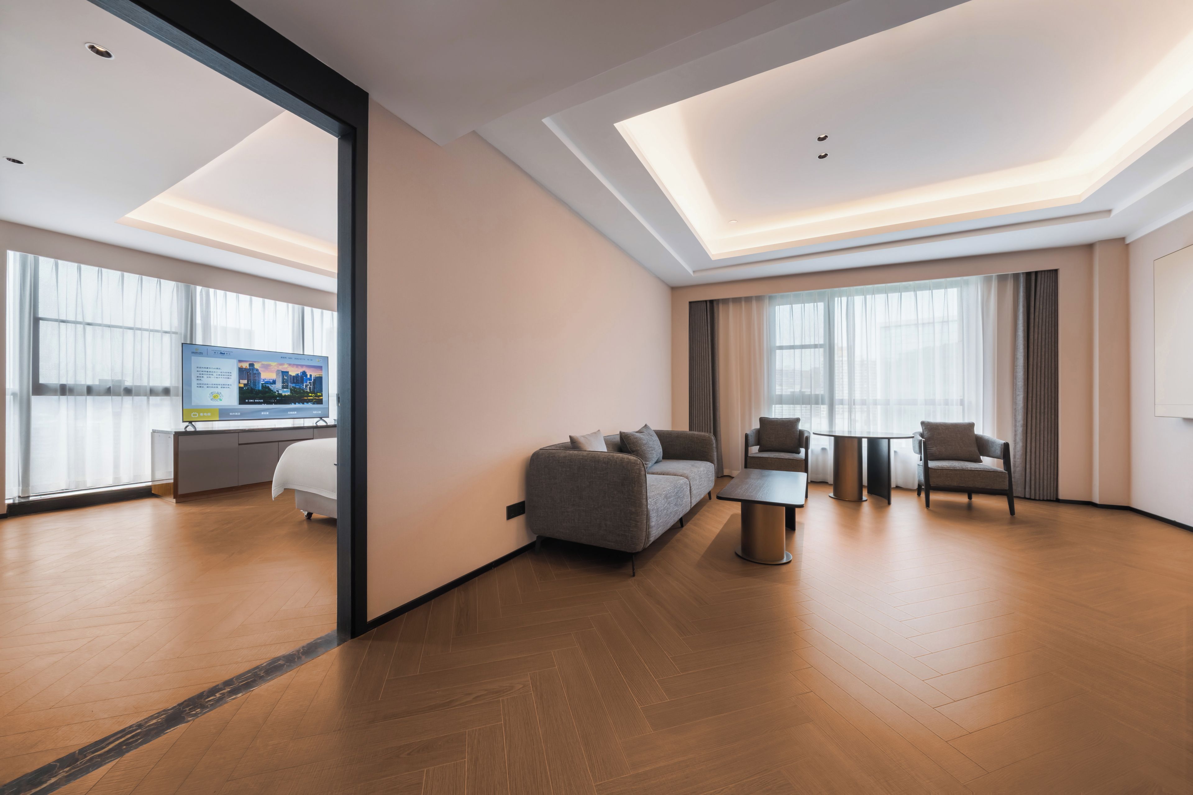 Une chambre d’hôtel moderne équipée d’un canapé, de fauteuils, d’une petite table et d’un téléviseur.