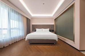 Una habitación de hotel moderna con una cama grande, una mesita de noche y un amplio ventanal con cortinas.