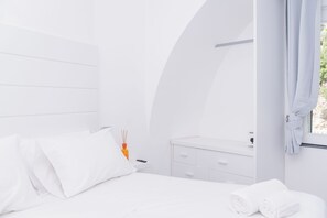 Une chambre à coucher moderne, aux tons clairs, comprenant un lit, une table de chevet, un miroir et une fenêtre avec des rideaux.