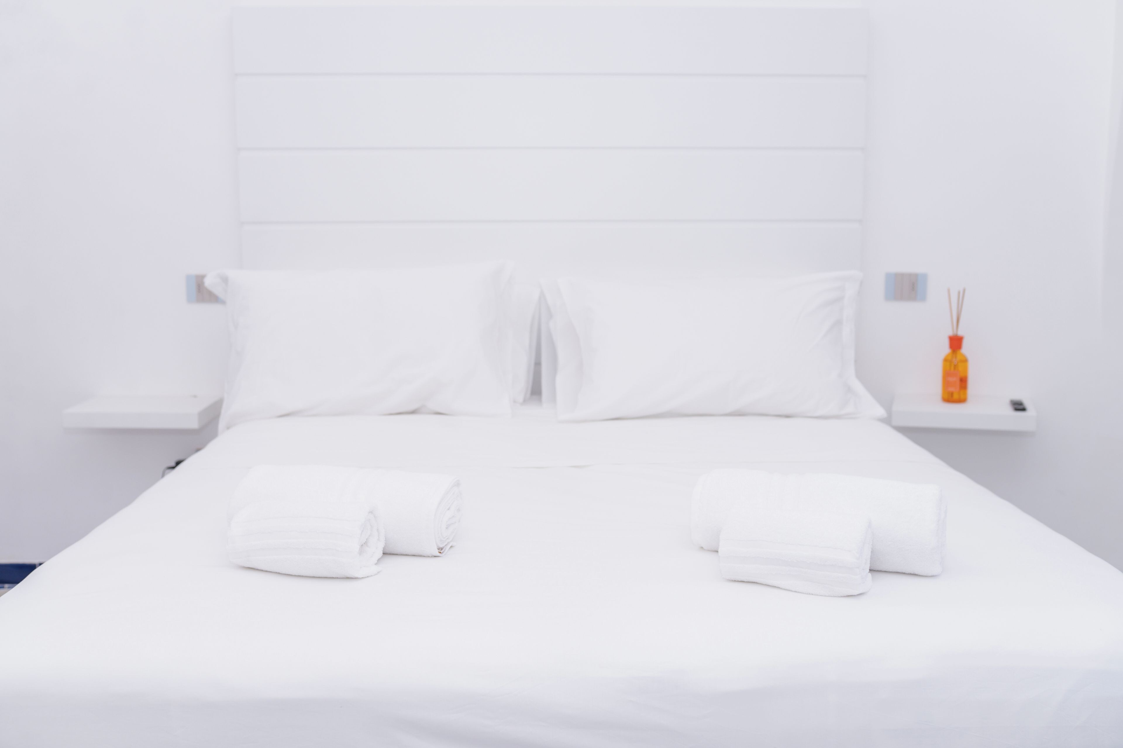 A neatly made bed with white linens and two rolled towels.