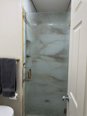 A bathroom with a glass shower door, a toilet, and a towel rack. - Cozy  studio in welcoming Indio with AC (Indio)