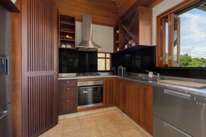 A modern kitchen with wooden cabinetry, stainless steel appliances, and a large window providing natural light. - Far Pavilions Villa A - Luxe Hillside Escape (Port Douglas)