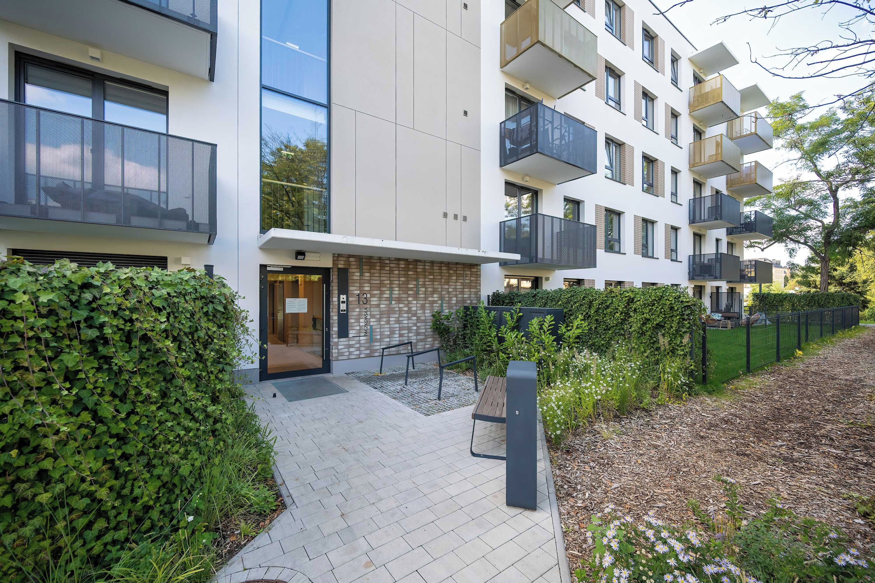 Ein modernes Apartmenthaus mit einer Steinfassade, mehreren Balkonen und einem geschlossenem Eingangsbereich.