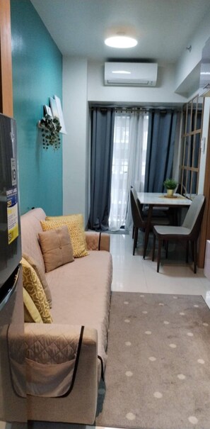 Uma sala de estar com sofá, mesa de jantar e cadeiras, e um aparelho de ar condicionado.