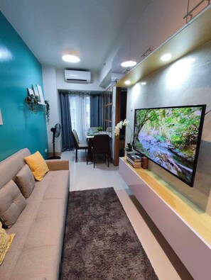 A living room with a sofa, a flat-screen TV, a dining table with chairs, and a small plant. - MOA Complex 1BR Shore 3 tower 1 unit 547 (Pasay City)
