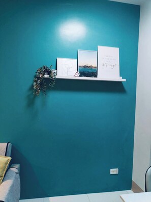 A teal-colored wall with a white shelf displaying framed artwork and a decorative plant. - MOA Complex 1BR Shore 3 tower 1 unit 547 (Pasay City)