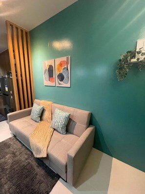 A modern living room with a beige sofa, two cushions, a throw blanket, and abstract wall art. - MOA Complex 1BR Shore 3 tower 1 unit 547 (Pasay City)