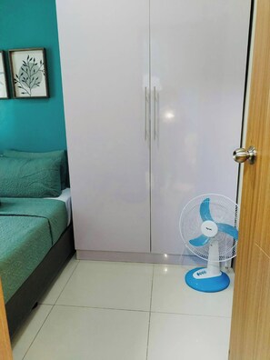 A bedroom with a bed, a wardrobe, and a standing fan. - MOA Complex 1BR Shore 3 tower 1 unit 547 (Pasay City)
