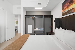 Ein modernes Hotelzimmer mit Bett, Schrank, Schreibtisch und einem Bild an der Wand.
