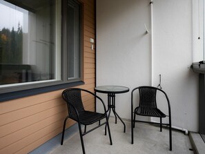Ein kleiner Sitzbereich im Freien mit zwei Stühlen und einem Tisch, neben einem Gebäude mit einem Fenster und einer Wandleuchte.