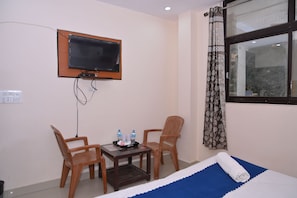Habitación de hotel con cama, televisor montado en la pared, una mesita con sillas y una ventana con cortinas.