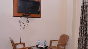 A hotel room with a bed, a TV mounted on the wall, a small table with two chairs, and a window with curtains.